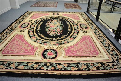Lot 1225 - A gross point carpet of European design, the charcoal field with an oval floral panel, framed...