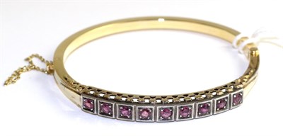Lot 38 - A ruby bangle, nine round cut rubies in white milgrain box settings, above a pierced gallery,...