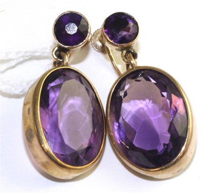 Lot 51 - A pair of amethyst earrings, a round cut amethyst suspends a larger oval cut amethyst in yellow...