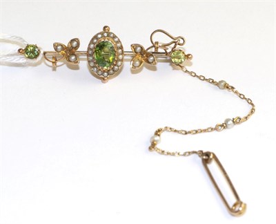 Lot 296 - A peridot and seed pearl bar brooch, an oval cut peridot in a yellow claw setting within a...