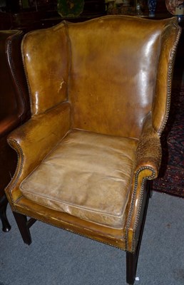 Lot 1295 - A 19th century wing armchair in George III stlye upholstered in worn leather, 78cm wide