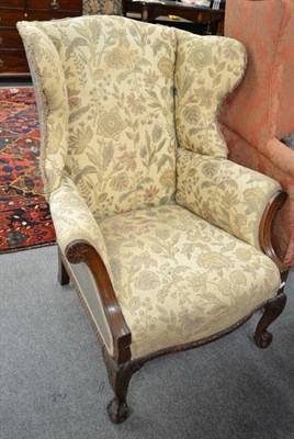 Lot 1298 - A mahogany framed wing armchair, upholstered in floral patterned fabric, carved arm supports, apron