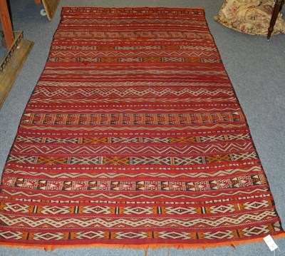 Lot 1302 - A Moroccan flat weave carpet, North West Africa, the madder field of narrowed polychrome bands...