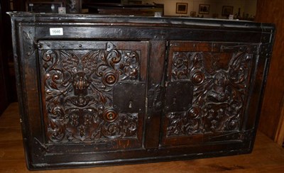 Lot 1646 - {} A carved oak wall cabinet with two cupboard doors carved in relief, with iron lock plates,...