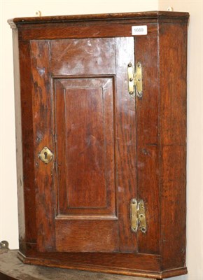 Lot 1669 - An 18th century oak hanging corner cupboard, fielded panel door with brass H shaped hinges...