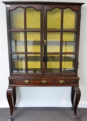 Lot 1685 - An oak glazed cabinet on stand, with two doors enclosing adjustable shelves, raised on a stand with