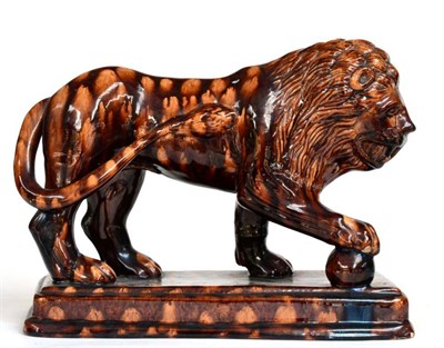 Lot 26 - ~ A Treacle Glazed Pottery Figure of a Lion, 19th century, its forepaw on a globe, on a stepped...