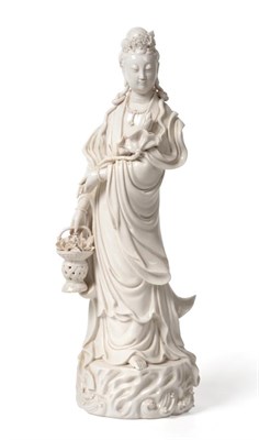 Lot 5 - A Blanc de Chine Figure of Guanyin, 18th/19th century, standing holding a flower and a basket...