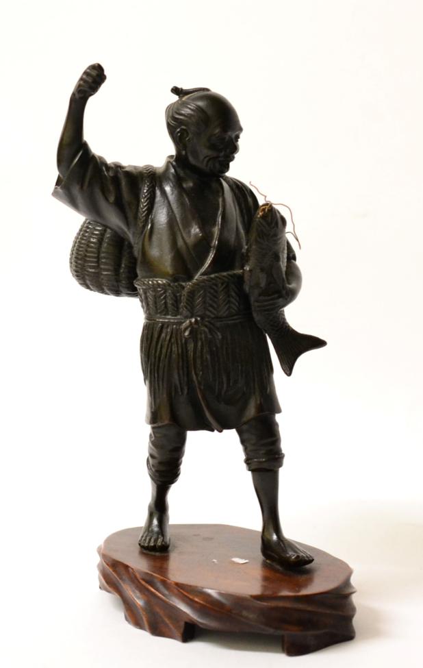 Lot 115 - A Japanese Bronze Figure of a Fisherman, Meiji period, standing holding a carp, his creel over...