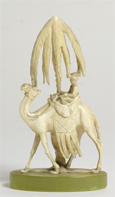 Lot 448 - A European Ivory Figure of a Bedouin Riding a Camel, early 20th century, standing before a palm...