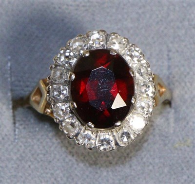 Lot 690 - An 18 Carat Gold Garnet and Diamond Cluster Ring, an oval cut garnet in a claw setting within a...