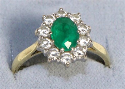 Lot 730 - An 18 Carat Gold Emerald and Diamond Cluster Ring, an oval cut emerald within a border of round...