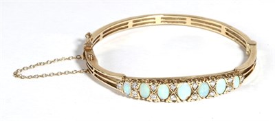 Lot 664 - A 9 Carat Gold Opal and Diamond Bangle, seven graduated oval cabochon opals spaced by pairs of...