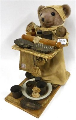 Lot 2009 - A Plush 'Baking' Teddy Bear mounted on a wooden plinth and holding a tray with baking cases,...
