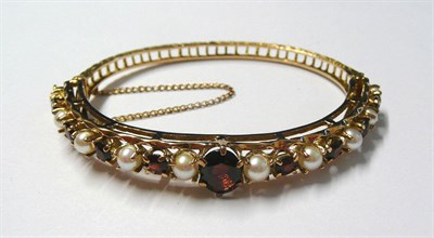 Lot 3 - A 9 Carat Gold Garnet and Cultured Pearl Bangle, an oval cut garnet centres a row of...