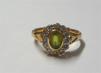 Lot 109 - A 14 Carat Gold Peridot and Diamond Cluster Ring, the oval mixed cut peridot in a yellow rubbed...