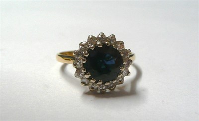 Lot 148 - An 18 Carat Gold Sapphire and Diamond Cluster Ring, the round brilliant cut sapphire within a...