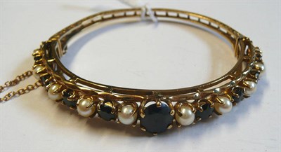 Lot 117 - A 9 Carat Gold Sapphire and Cultured Pearl Bangle, a central oval mixed cut sapphire to a row...