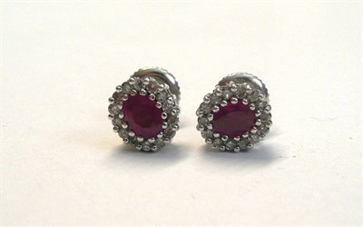 Lot 122 - A Pair of 18 Carat White Gold Ruby and Diamond Stud Earrings, each with an oval cut ruby within...