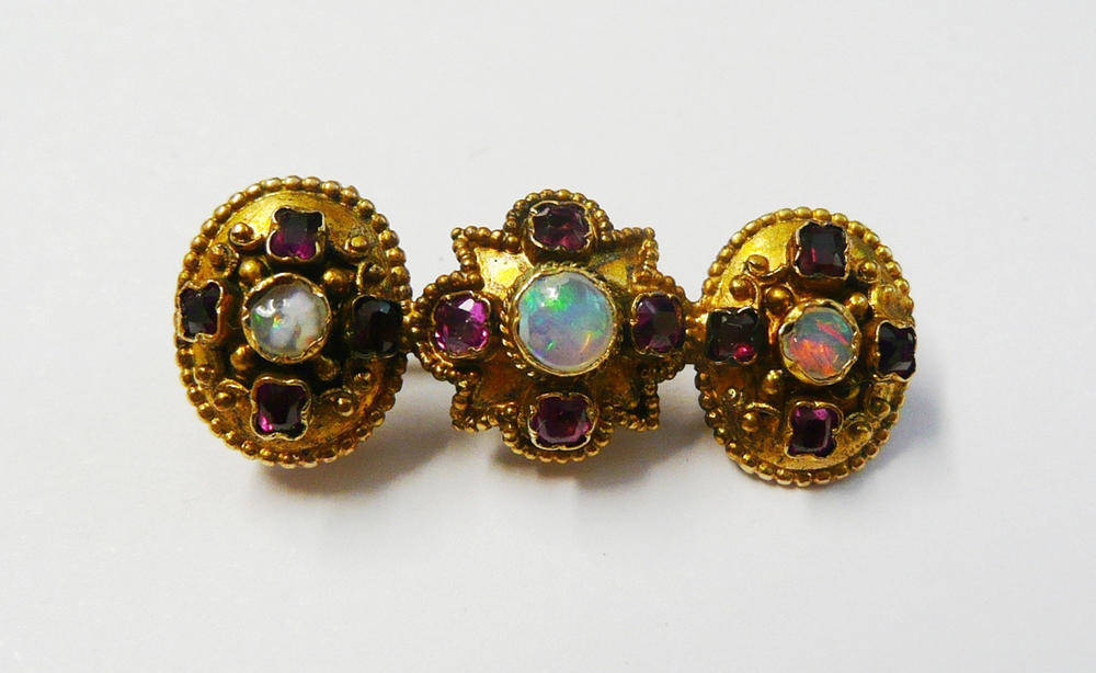 Lot 166 - An Opal and Ruby Bar Brooch, a star shape flanked by two ovals, each set with a cabochon opal...