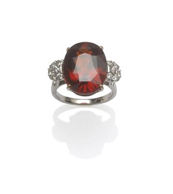 Lot 1055 - An 18 Carat White Gold Garnet and Diamond Ring, the oval mixed cut garnet flanked by a cluster...