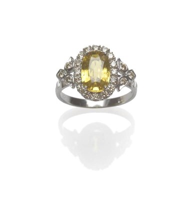 Lot 1094 - An 18 Carat White Gold Yellow Sapphire and Diamond Ring, the oval mixed cut sapphire within a...