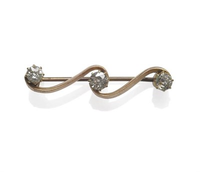 Lot 1125 - A Diamond Three Stone Brooch, the old cut stones in yellow claw settings, on a scroll bar,...