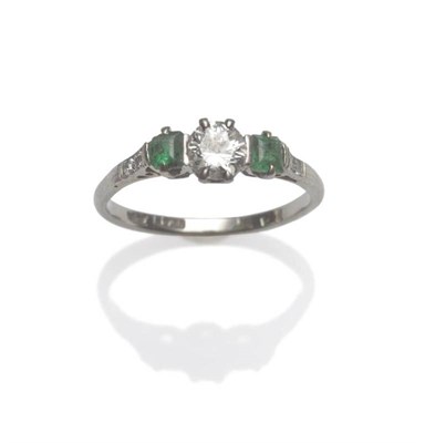 Lot 1187 - A Diamond and Emerald Three Stone Ring, a round brilliant cut diamond between two square step...