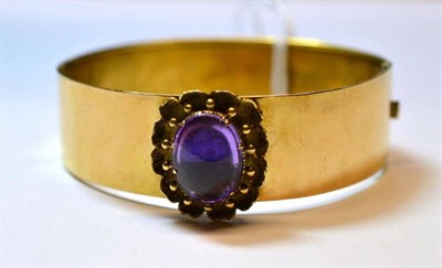 Lot 1192 - A Bangle, the broad plain polished yellow bangle, set with a cabochon amethyst in a floral...