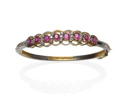 Lot 1064 - A Ruby and Diamond Set Two Colour Bangle, half hinged with oval cut rubies alternating with rows of