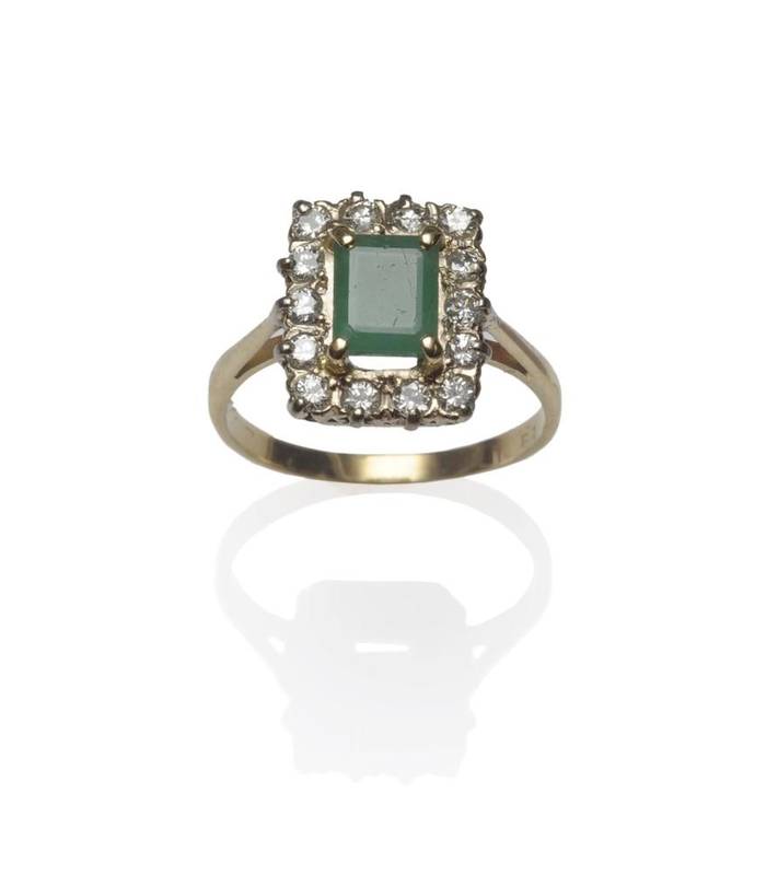 Lot 1087 - An 18 Carat Gold Emerald and Diamond Cluster Ring, the step cut emerald in yellow claw...