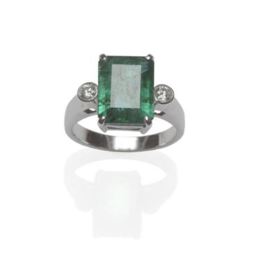 Lot 1089 - An Emerald and Diamond Three Stone Ring, the emerald-cut emerald in a white four claw setting, with