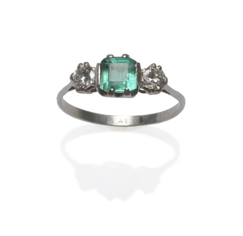 Lot 1096 - An Emerald and Diamond Three Stone Ring, the step cut emerald with truncated corners flanked by...