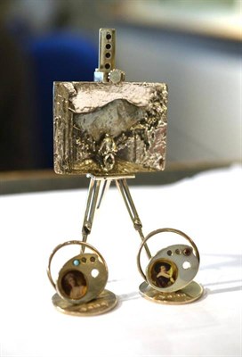 Lot 1308 - A Novelty Silver Miniature Artists Easel and Painting, marked MEDUSA.ORO, with folding legs and...