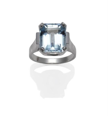 Lot 1144 - An Aquamarine Ring, the emerald-cut aquamarine in a white four claw setting to a broad...