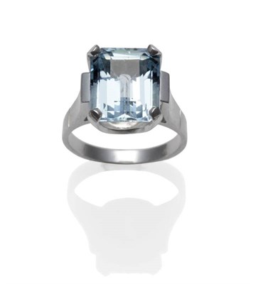 Lot 1098 - An Aquamarine Ring, the emerald-cut aquamarine in a white four claw setting to a broad...