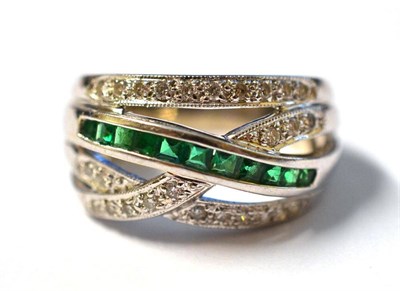 Lot 1151 - An Emerald and Diamond Crossover Ring, inset with step cut emeralds and round brilliant cut...