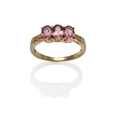 Lot 1187 - An 18 Carat Gold Padparadscha Three Stone Ring, the oval mixed cut padparadscha sapphires in yellow