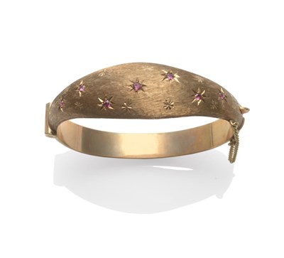 Lot 2100 - A 9 Carat Gold Bangle, hinged with a textured tapered front with star motifs, and inset with rubies