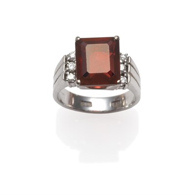 Lot 2074 - A Garnet and Diamond Ring, an emerald-cut garnet in a white four claw setting, three diamonds...