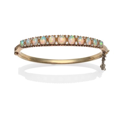 Lot 2107 - An Opal and Diamond Bangle, circa 1910, eleven graduated oval cabochon opals with pairs of old...