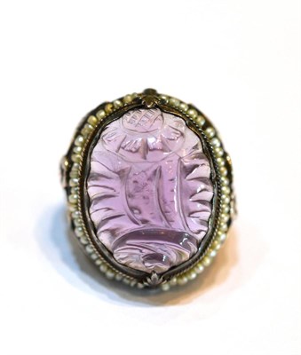 Lot 2031 - A Carved Amethyst and Seed Pearl Dress Ring, a foliate carved oval cabochon amethyst in a white...