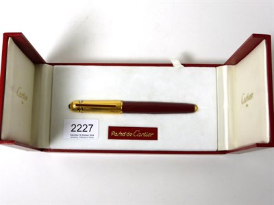 Lot 2227 - Cartier: A Pasha de Cartier Ballpoint Pen, with a red barrel and gilt cap, in original box with...