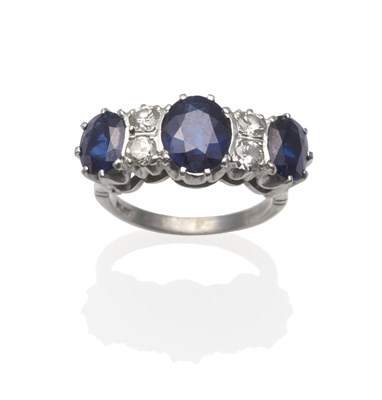 Lot 2019 - A Sapphire and Diamond Ring, three graduated oval mixed cut sapphires spaced by pairs of...