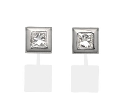 Lot 2001 - A Pair of 18 Carat White Gold Princess Cut Diamond Solitaire Earrings, in a broad square rubbed...