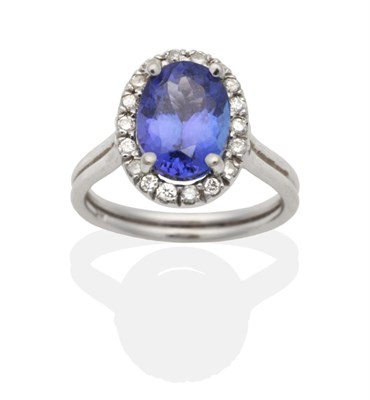 Lot 2028 - A Tanzanite and Diamond Cluster Ring, an oval cut tanzanite in a claw setting, within a border...