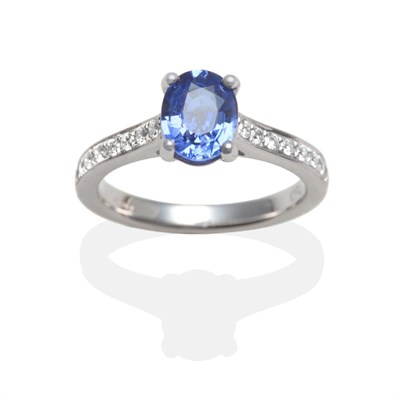 Lot 2037 - An 18 Carat White Gold Sapphire and Diamond Ring, an oval cut sapphire in a claw setting, to...