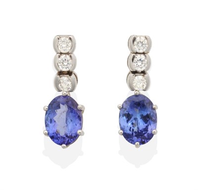 Lot 2123 - A Pair of Tanzanite and Diamond Drop Earrings, a line of three round brilliant cut diamonds in half