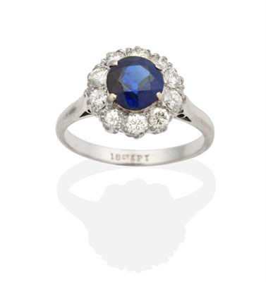 Lot 2130 - A Sapphire and Diamond Cluster Ring, a round cut sapphire within a border of round brilliant...