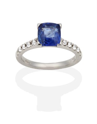 Lot 2146 - An 18 Carat White Gold Sapphire and Diamond Ring, a cushion cut sapphire in a claw setting, to...